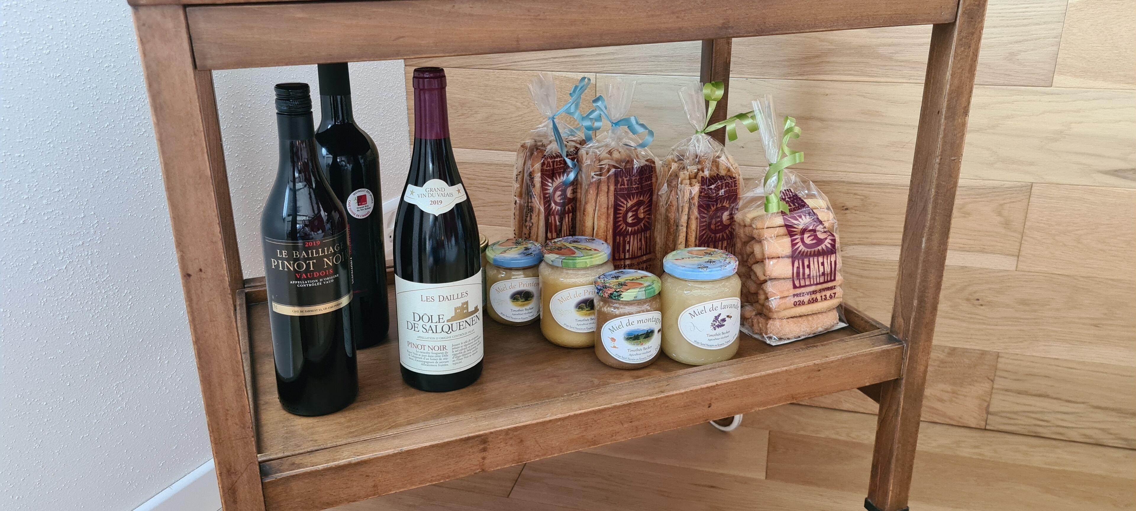 A wooden shelf with bottles of wine, jars of preserves, and packaged bread.
