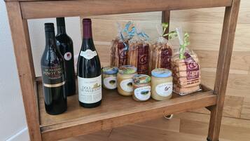 A wooden shelf with bottles of wine, jars of preserves, and packaged bread.