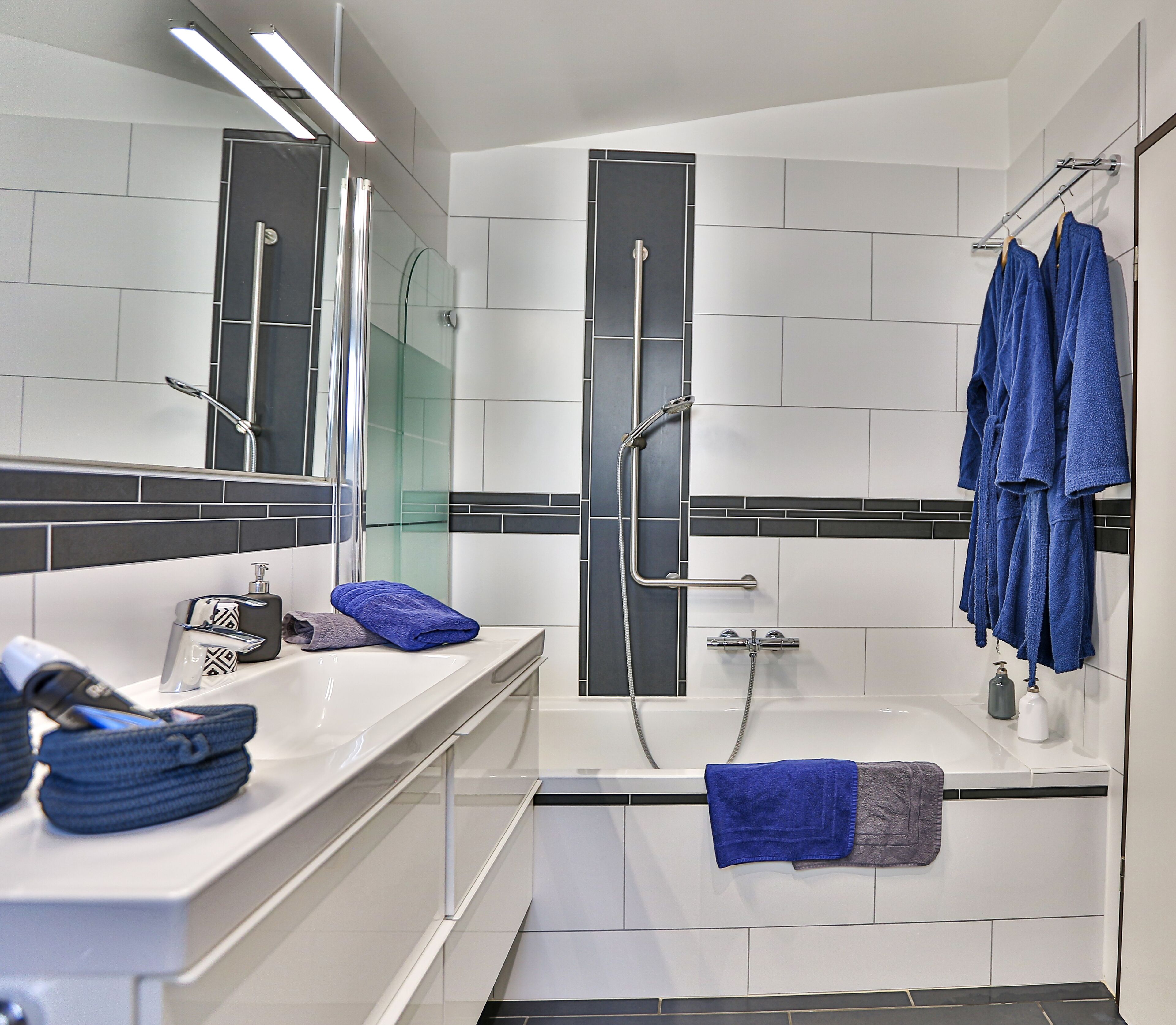 A modern bathroom with a bathtub, a shower, and a vanity with a mirror. There are towels and toiletries on the counter.