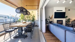 Ein modernes Wohnzimmer mit Holzboden, einem Esstisch mit Stühlen, einem blauen Sofa und einem an der Wand befestigten Fernseher.