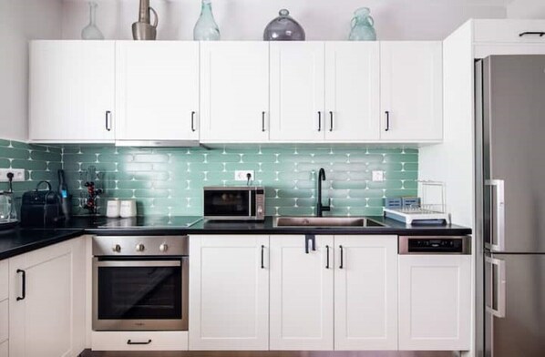 A modern kitchen with white cabinets, a green backsplash, stainless steel appliances, and a black countertop.