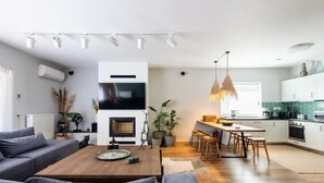 Ein modernes Wohnzimmer mit Kamin, Essbereich und einer Küche mit weißen Schränken und einer grünen Spritzschutzwand.