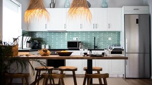 Eine moderne Küche mit weißen Schränken, einer zentralen Kochinsel mit Barhocker, einem Edelstahl-Kühlschrank und einer grünen Fliesenrückwand.