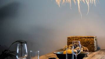 A dining table with a woven pendant light fixture, clear glasses, and a basket of lemons.