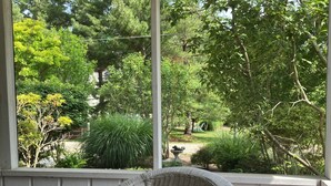 A wicker chair with a cushion on a porch overlooking a garden with various trees and shrubs. - Charming 3-bedroom cottage in enjoyable Douglas with WiFi, AC (Douglas)