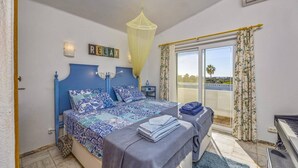 A bedroom with a bed, a small table, a piano, and a view of the outside. - Villa Casa Fatinha by Villa Plus (Praia do Carvoeiro)