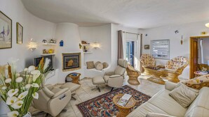 A spacious living room with a fireplace, comfortable seating, decorative wall art, and a large window. - Villa Casa Fatinha by Villa Plus (Praia do Carvoeiro)