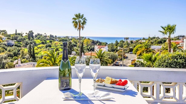 A table with a bottle of champagne, two glasses, and a plate with snacks on a balcony overlooking a coastal landscape. - Villa Casa Fatinha by Villa Plus (Praia do Carvoeiro)