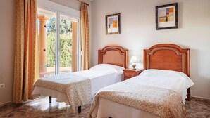 Ein Hotelzimmer mit zwei Betten, einem großen Fenster mit Vorhängen, einem Holzkopfende und zwei gerahmten Bildern an der Wand.