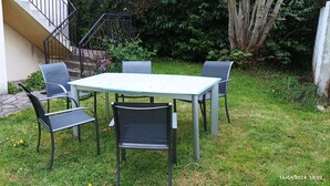 En uteplats med ett bord och fyra stolar, ett litet fönster och en trappa som leder upp till en balkong.