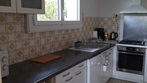 Ett kök med vita skåp, en svart bänkskiva, ett fönster, en spis och en kakelbeklädd vägg bakom arbetsbänken.
