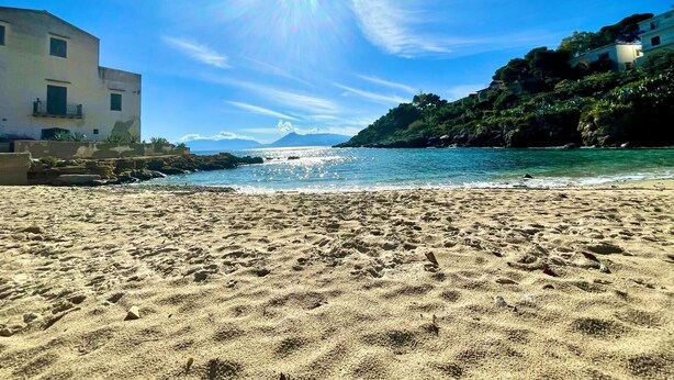A beach with a clear sky, rocky shoreline, and buildings on the left. - Stunning apartment only 100 meters from the sea and spectacular gulf view. (Santa Flavia)