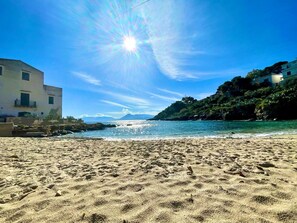 Una playa con cielo despejado, costa rocosa y edificios a la izquierda.