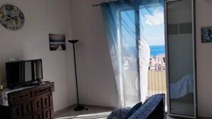A room with a TV on a wooden cabinet, a floor lamp, a chair, a balcony with a view of the sea, and two wall art pieces. - Stunning apartment only 100 meters from the sea and spectacular gulf view. (Santa Flavia)
