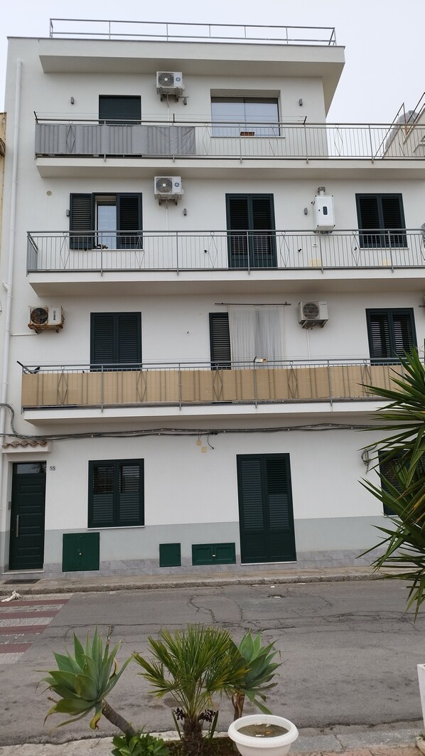 Un edificio de varios pisos con balcones, unidades de aire acondicionado y una entrada con portón.