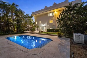 A modern house with a swimming pool, surrounded by lush greenery and palm trees.