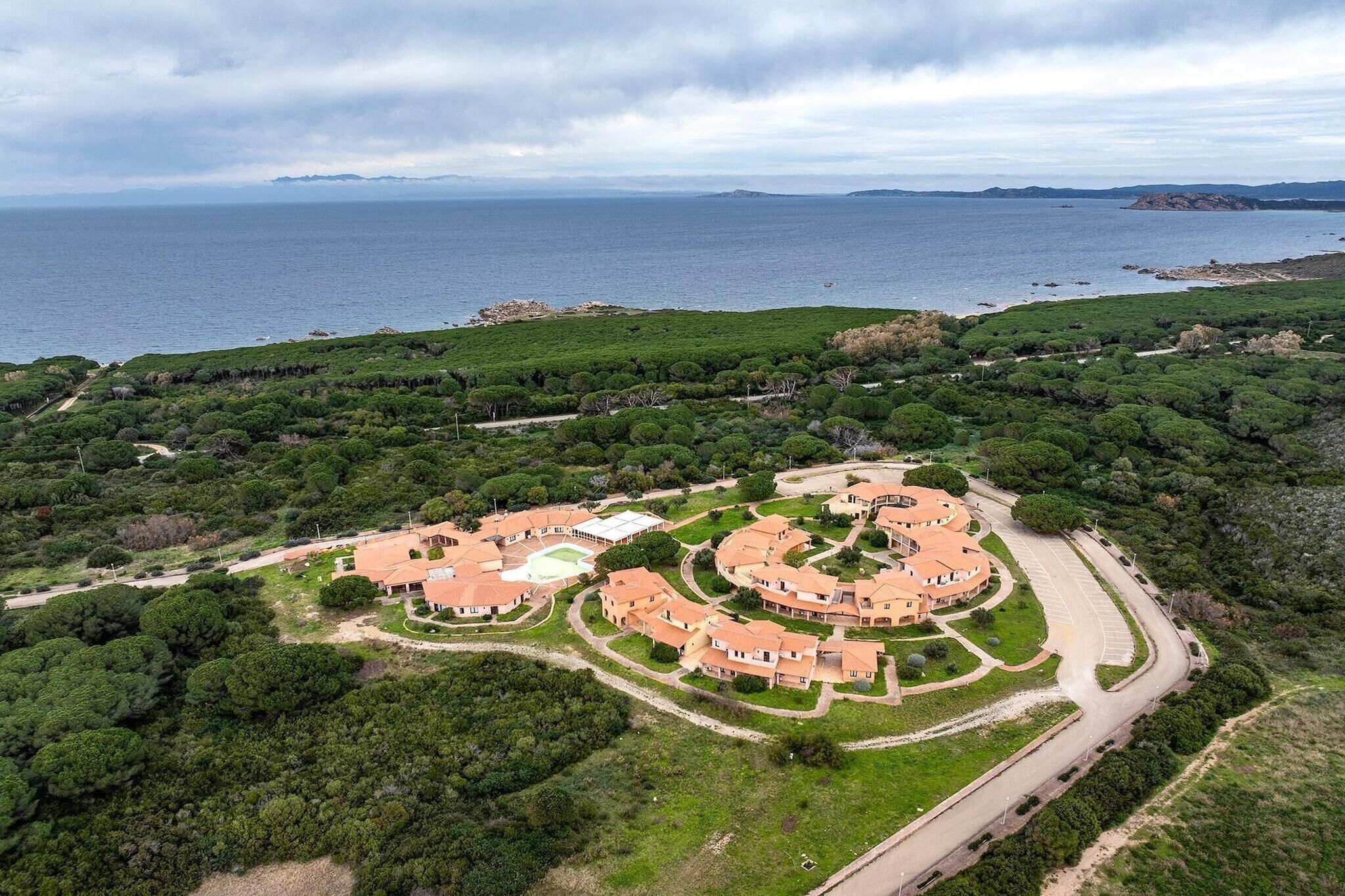 A coastal property with a circular layout of buildings, surrounded by dense greenery and a view of the sea.