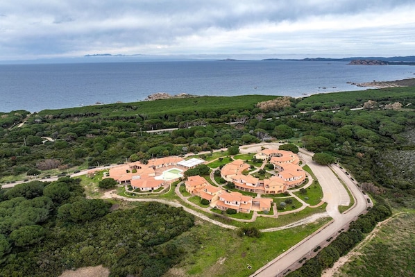 A coastal property with a circular layout of buildings, surrounded by dense greenery and a view of the sea.