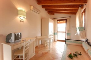 A room with a kitchenette, a dining area, a sofa, and a window with curtains.