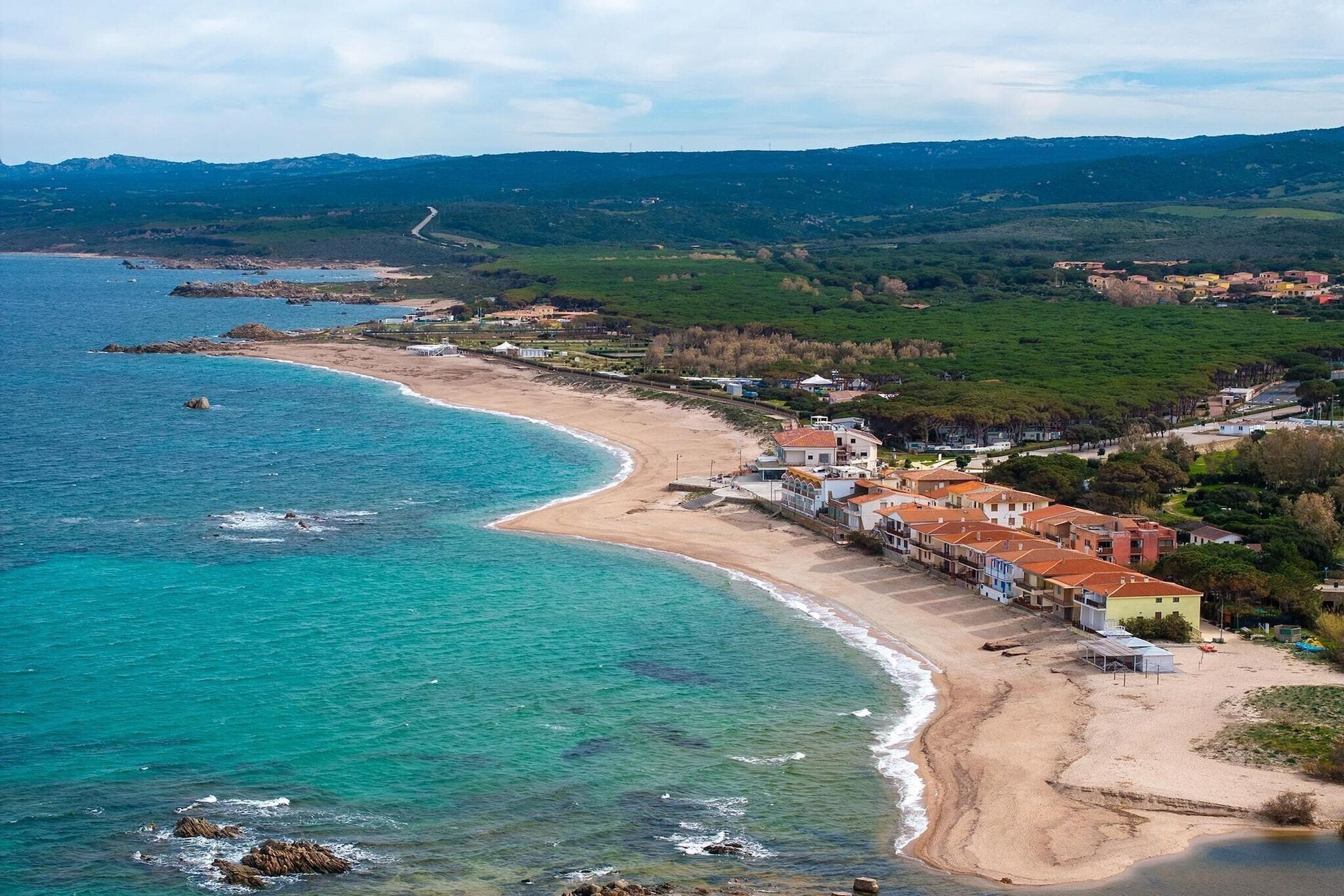 A coastal town with a beach, buildings, and a hilly landscape in the background.