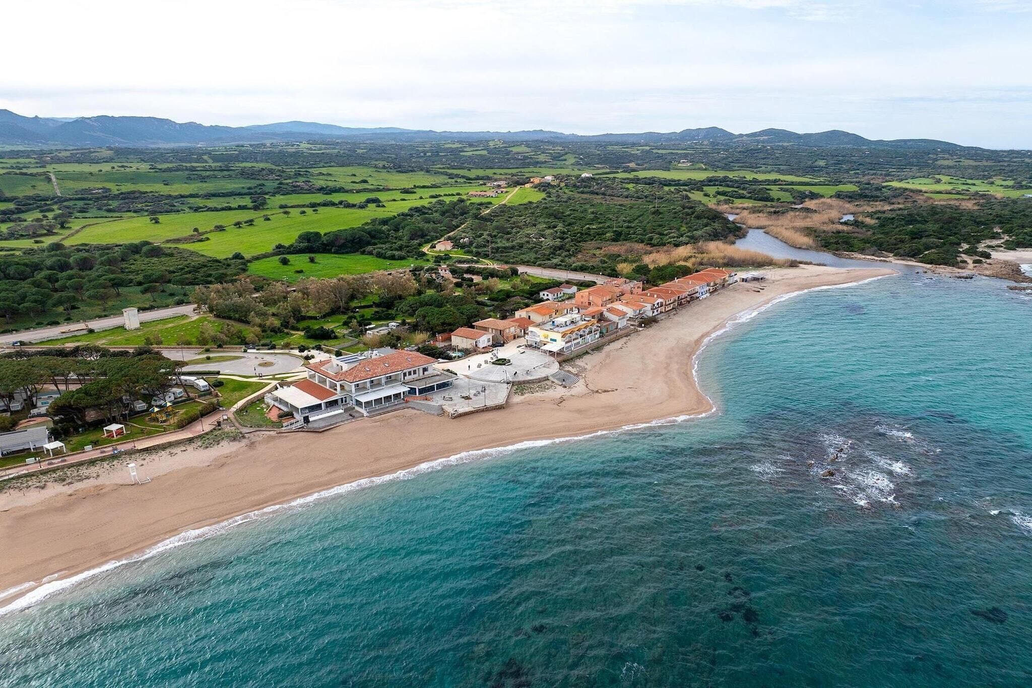An aerial view of a coastal town with a beach, houses, and green fields.