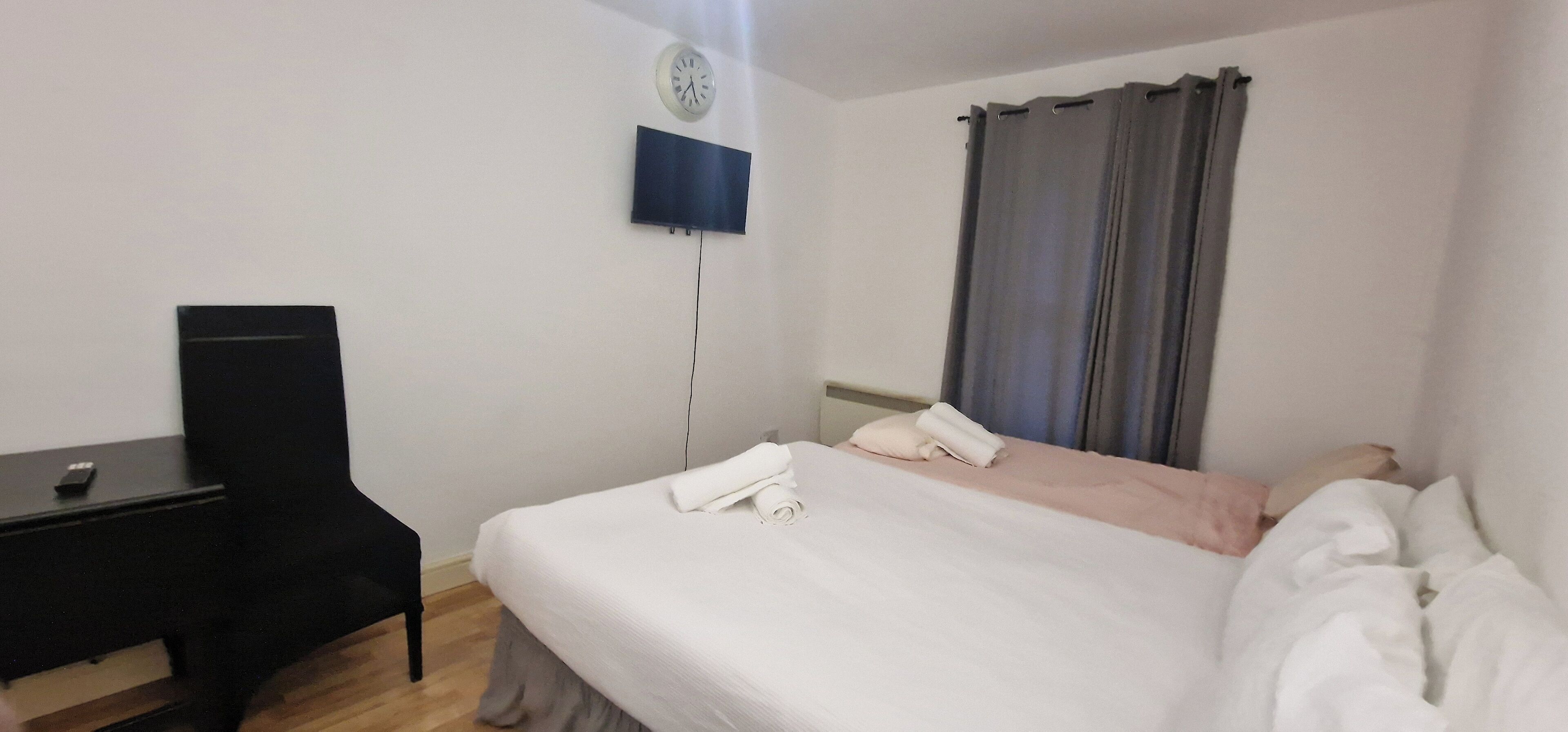 A hotel room with a bed, a desk, a chair, a TV mounted on the wall, and a window with curtains.