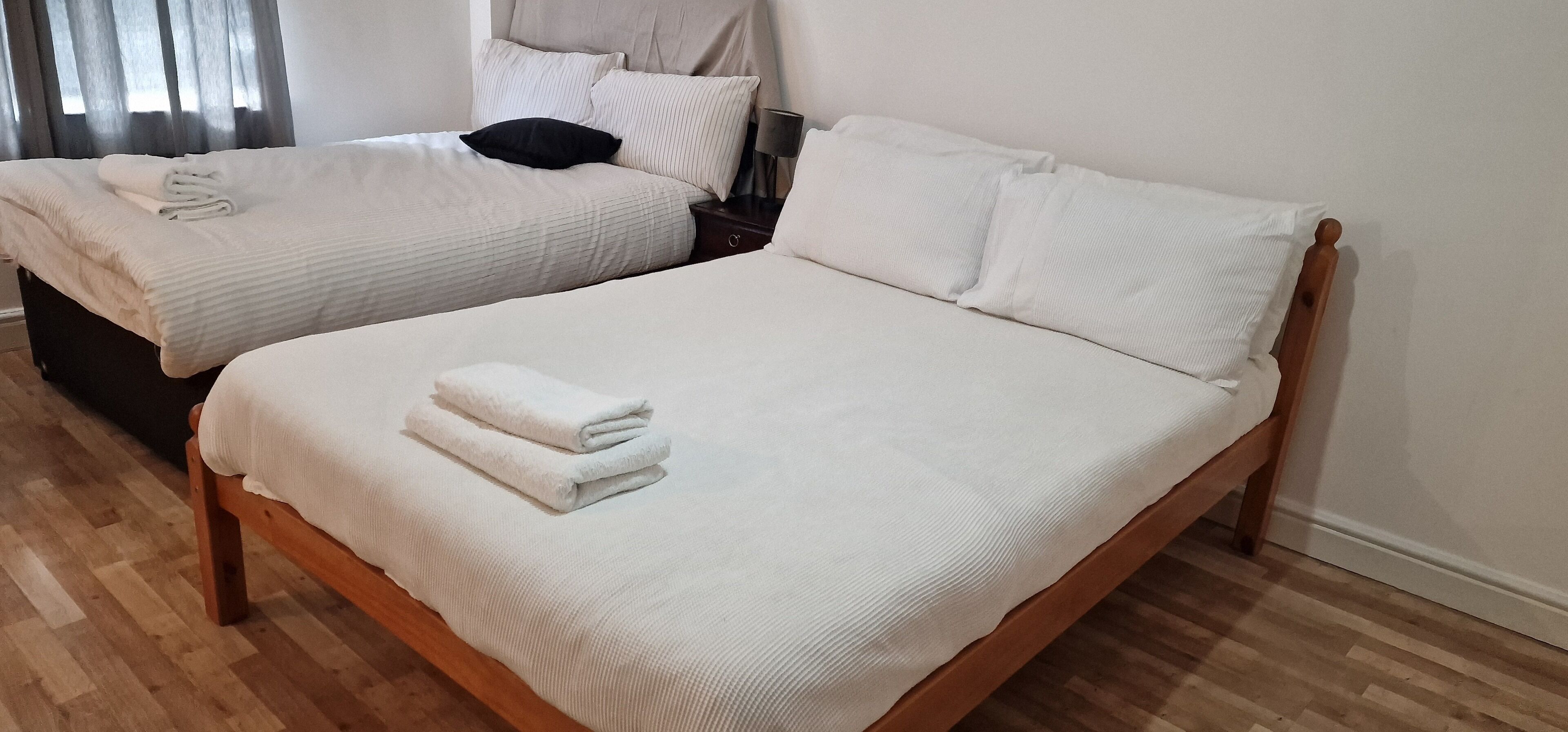 Two single beds with white linens and pillows, a wooden headboard, and a nightstand with a lamp.