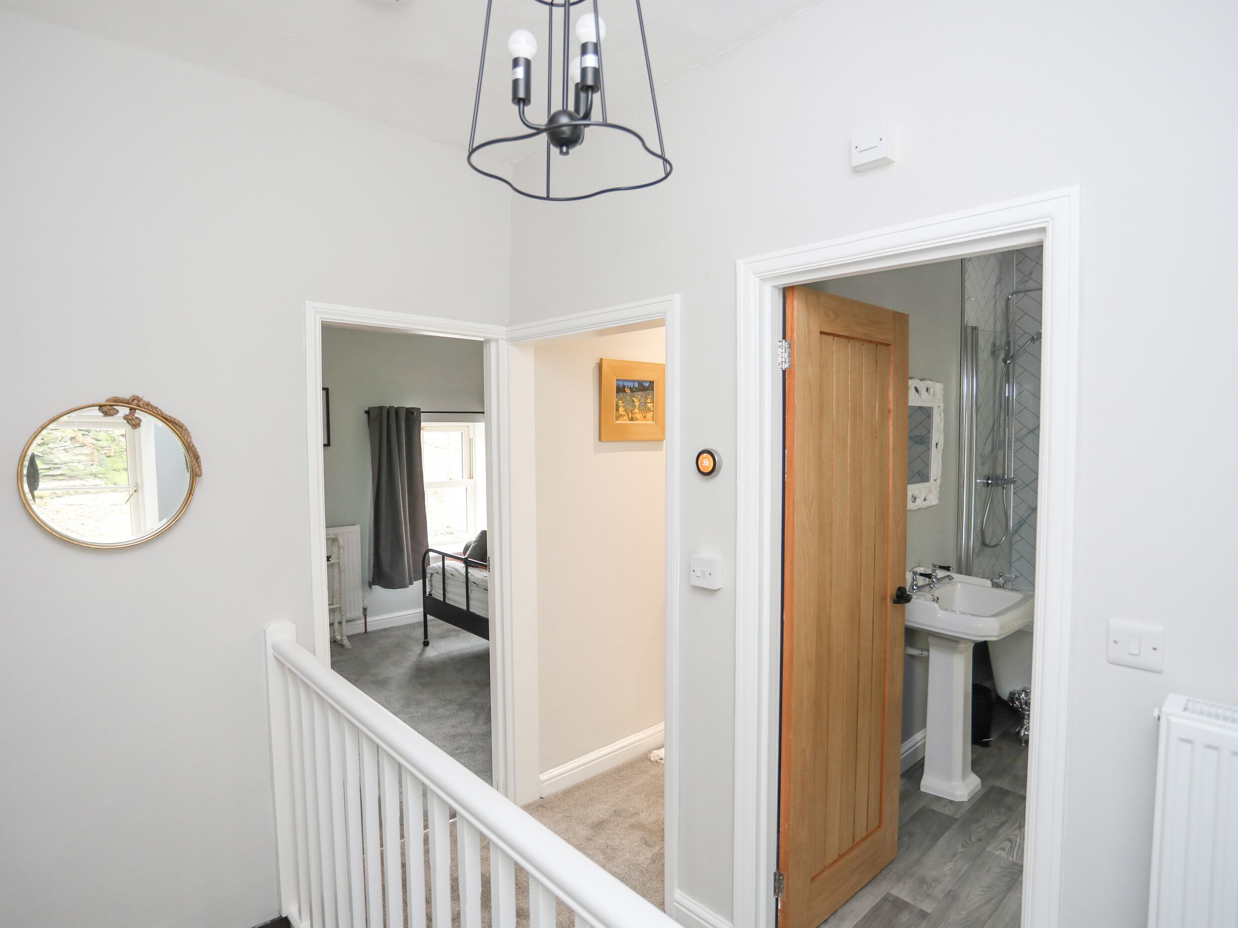 A hallway with a white railing, a wooden door leading to a bathroom, and a mirror on the wall.