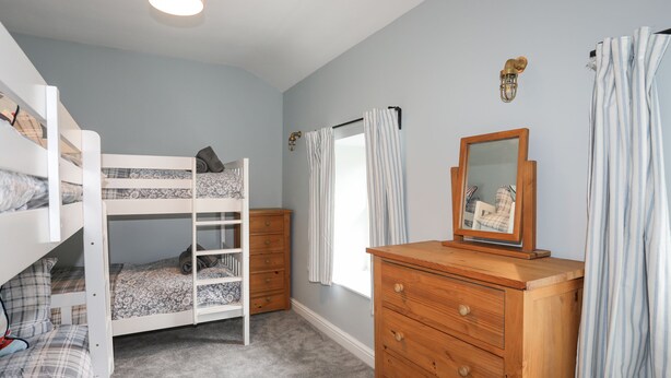 Une chambre d’enfant avec des lits superposés, une commode, un miroir et une fenêtre avec des rideaux.