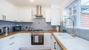 Een moderne keuken met witte kasten, een roestvrijstalen afzuigkap, een inbouwoven, een magnetron, een gasfornuis en een groot raam met zonwering.