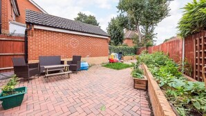 Een terras van bakstenen met tuinmeubilair, een bloembed en een houten omheining.