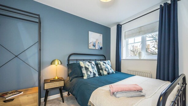 Een slaapkamer met een bed, nachtkastje, lamp en een raam met gordijnen.