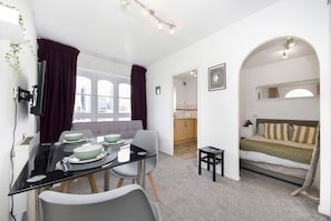 Cozy retreat with a dining area for four, a comfortable sofa, and a bed with a striped blanket.