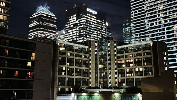 A nighttime cityscape with modern high-rise buildings, including a prominent building with illuminated signage. - The Canary Hub based in Canary Wharf (Greater London)