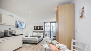 A modern hotel room with a bed, a dining table with plates, a TV, and a view of the city. - The Canary Hub based in Canary Wharf (Greater London)