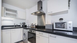 A modern kitchen with white cabinets, a stainless steel range hood, a built-in oven, a microwave, and a washing machine. - The Canary Hub based in Canary Wharf (Greater London)