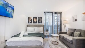 A modern hotel room with a bed, a sofa, a small table, and a TV. - The Canary Hub based in Canary Wharf (Greater London)