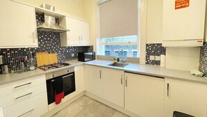 A modern kitchen with white cabinets, a black stove, and a window with a view of buildings. - Kings X & Angel Haven (Greater London)
