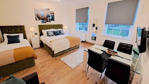A modern bedroom with two beds, a dining area, and a TV. - Kings X & Angel Haven (Greater London)