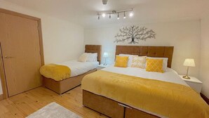 A bedroom with two beds, a wooden wardrobe, a white rug, and a wall-mounted tree decoration. - Kings Cross St Pancras Oasis (Greater London)