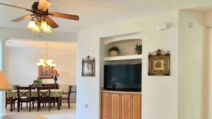 A living room with a dining area, a ceiling fan, a flat-screen TV, and wooden cabinets.