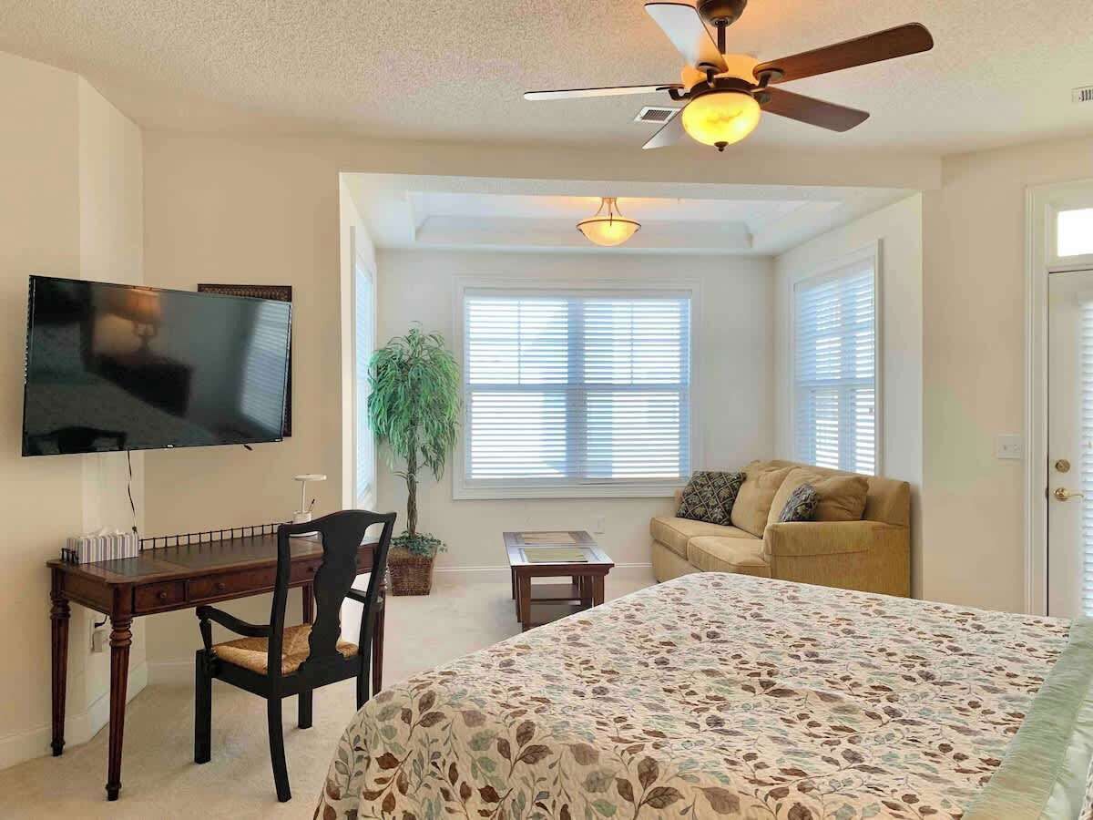 Une chambre à coucher comprenant un lit, un bureau, une chaise, un téléviseur et un ventilateur de plafond.