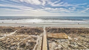 A beach with a wooden boardwalk leading to a wooden structure, a sandy beach, and the ocean.