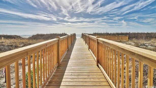 A wooden boardwalk leading to the beach with railings on both sides.