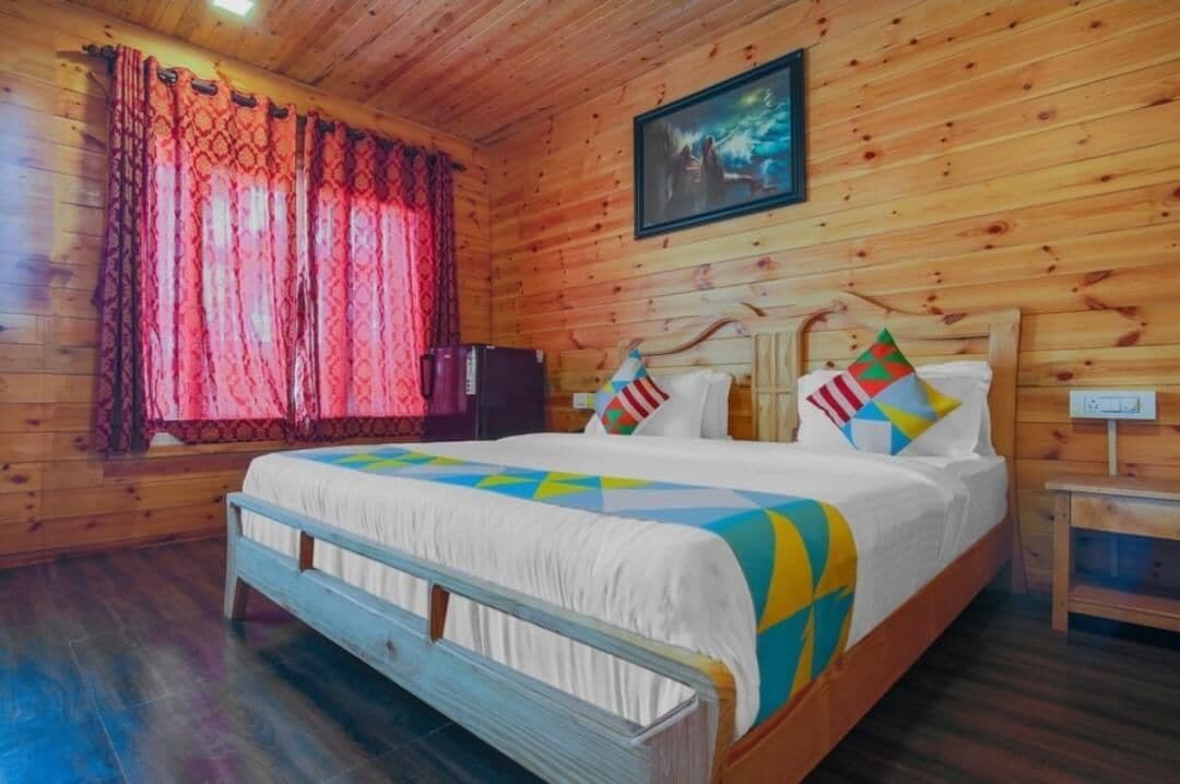 A wooden cabin room with a bed, curtains, a painting, and a nightstand.