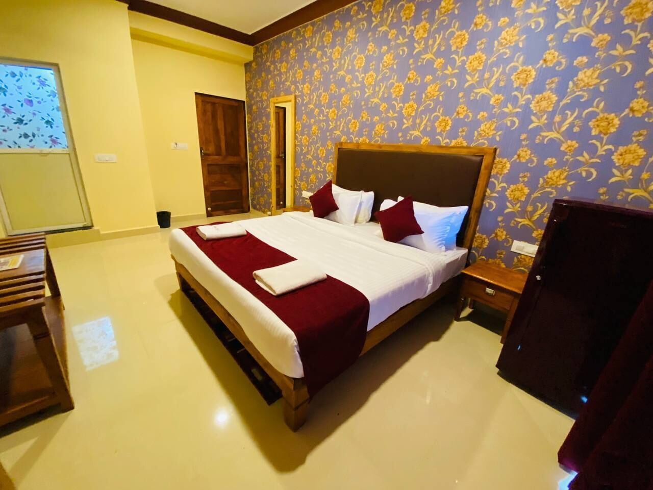 A hotel room with a large bed, wooden headboard, and a floral wallpaper pattern.