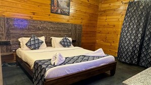 A wooden cabin bedroom with a bed, a nightstand, a wall-mounted heater, and a window with a view of a bridge. - OZIBA BEACH RESORT (Arambol)