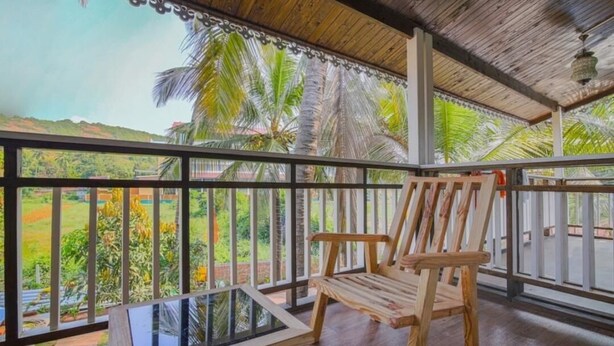 A wooden deck with a glass table and chair, overlooking a lush landscape with palm trees. - OZIBA BEACH RESORT (Arambol)