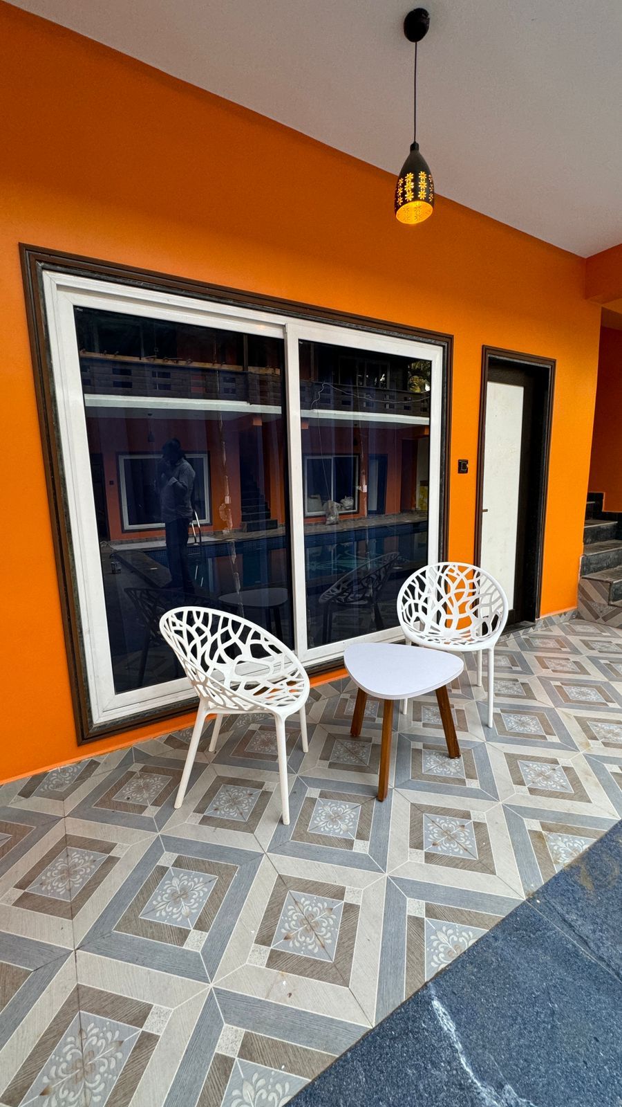 Quarto com uma janela grande, duas cadeiras brancas e um lustre.