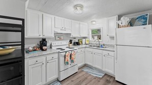 A compact kitchen with white cabinets, a stove, a sink, and a refrigerator. - Jax Bch Home 3/2 w/Pets (Jacksonville Beach)